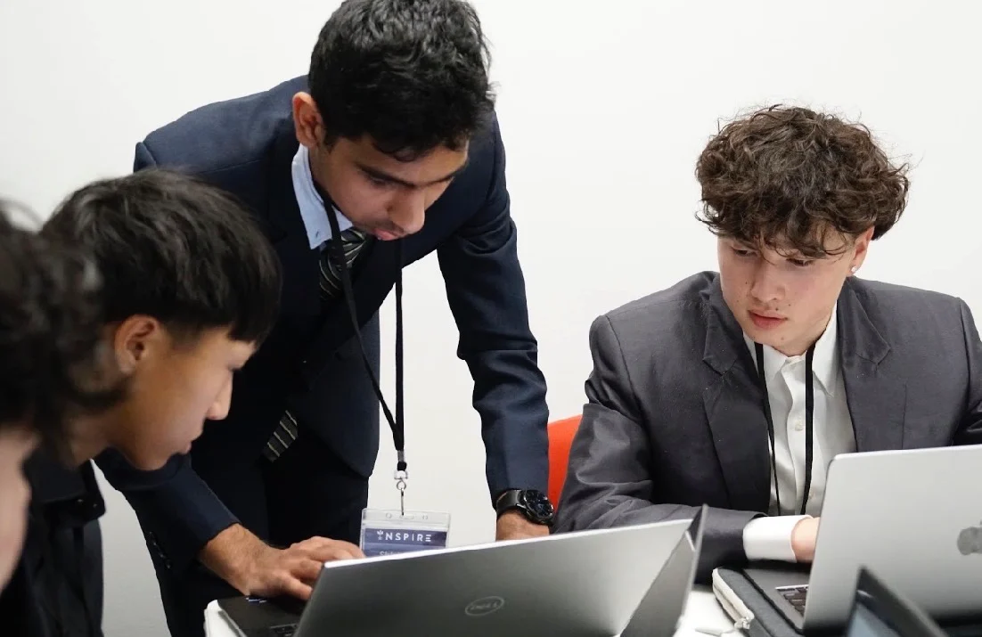 Two students working on a laptop while a teammate leans in